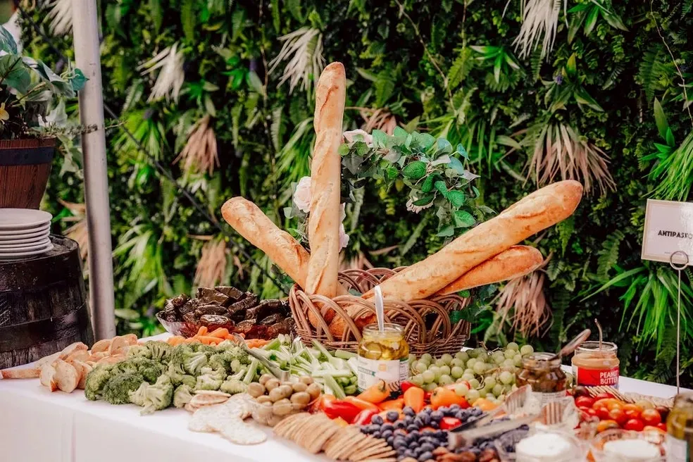 An overflowing antipasto and charcuterie catering spread of breads, cheeses, fruit and vegetables